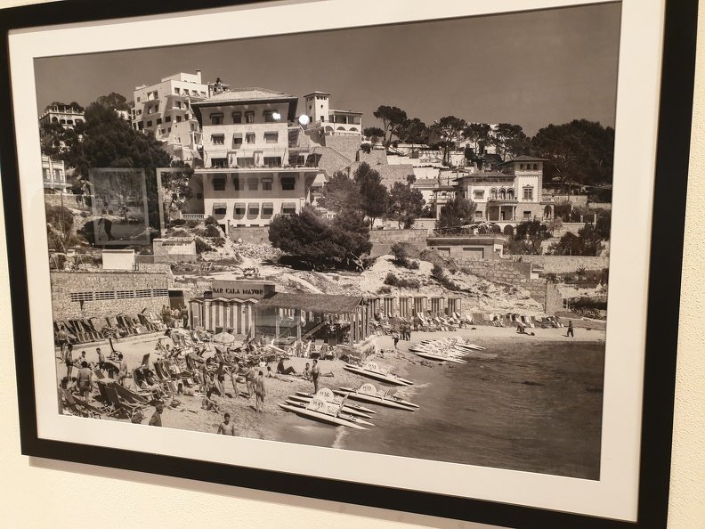 Cala Major, located in Palma, Mallorca, appears in this vintage photograph as a tranquil and picturesque seaside getaway. The monochromatic tones capture the charm of a bygone era, characterized by classic Mediterranean architecture and a relaxed beach atmosphere. Visitors are seen enjoying the sun, with rows of sun loungers spread along the sandy shore and calm waters inviting a leisurely swim. 20210611_132649.jpg