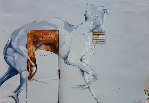 Mural de un caballo azul pálido sobre una pared gris.