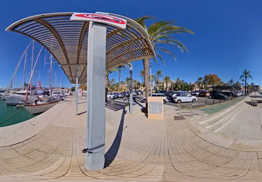 Barche a vela accanto a un porto turistico fiancheggiato da palme
