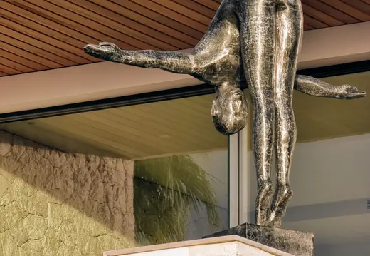 Scultura di una figura piegata con le braccia distese