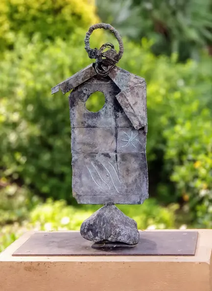Abstract bronze sculpture in a blurred garden.webp