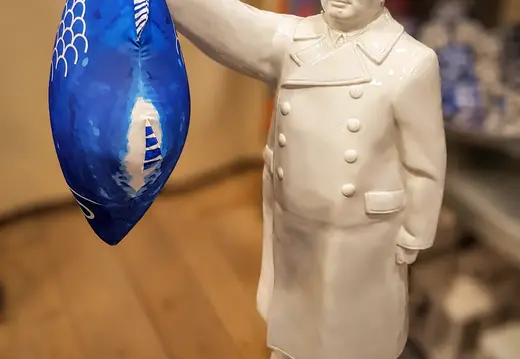 Weiße Keramikfigur hält einen blauen Fischsack