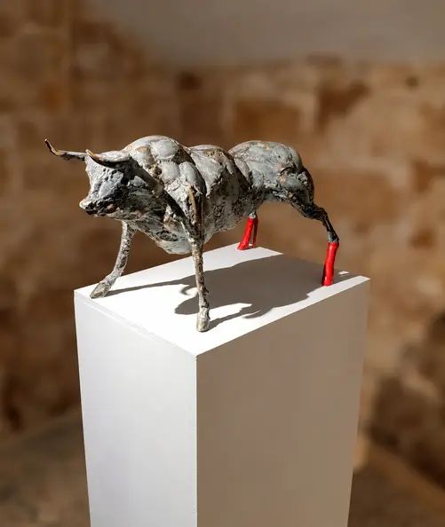 Metallic bull sculpture with blurred stone walls.webp