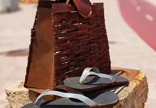 Metallhandtasche und Flip-Flops auf einer Steinbasis