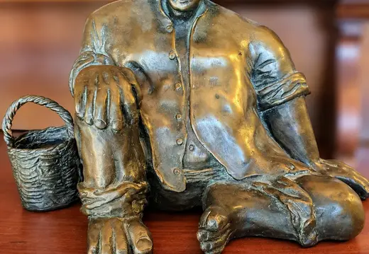Sitzende Figur mit Hut und Korb