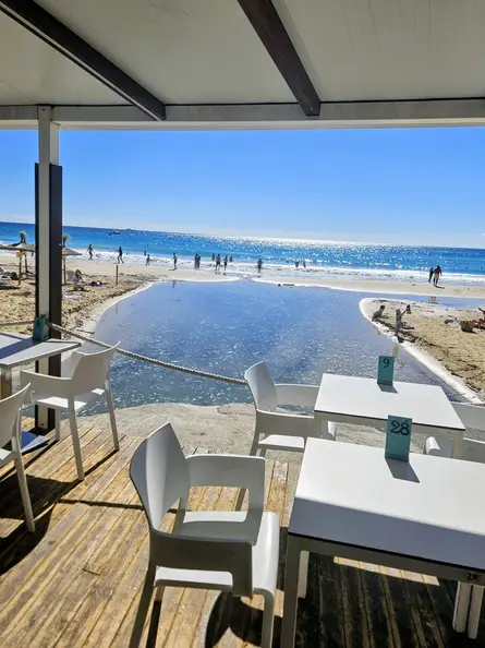 Shaded beach‑restaurant terrace overlooking Cala Major beach and glittering Mediterranean sea.