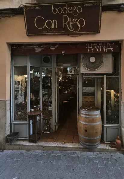 Entrance and wooden sign of Bodega Ca'n Rigo wine bar with barrel and stools